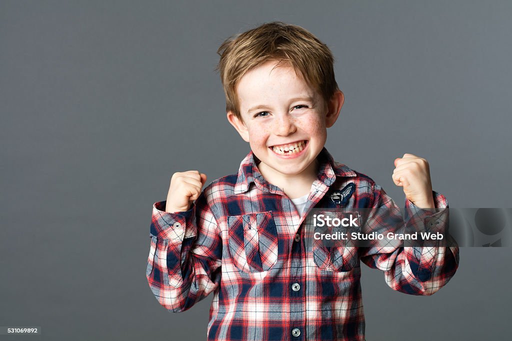 winning young child with tooth missing raising arms for excitement winning kid - winning young red hair child with a tooth missing raising his arms for happiness and excitement, grey background studio Child Stock Photo
