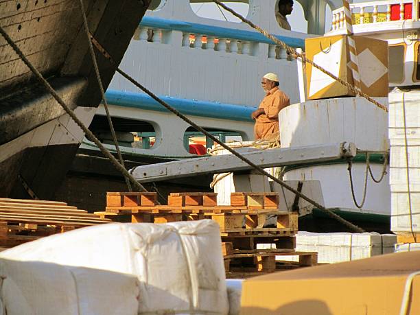 Dubai, United Arab Emirates - October 20, 2010: An Arabian man is standing on a boat in the harbour of Dubai, United Arab Emirates. Several boats are visible and some goods are waiting to be transported.