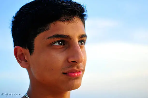 A closeup of a young man, against a blue sky.