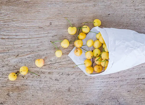Yellow sweet-cherries in a paper bag on a rough wood background