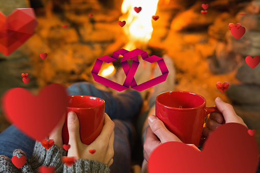 Hands with red coffee cups in front of lit fireplace against linking hearts