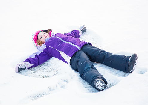 Young girl laying in the fresh snow making a snow angel.