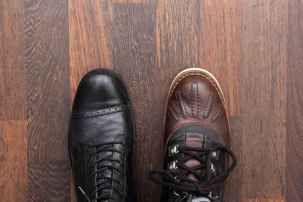 Pair of different mens leather boots on parquet stock photo