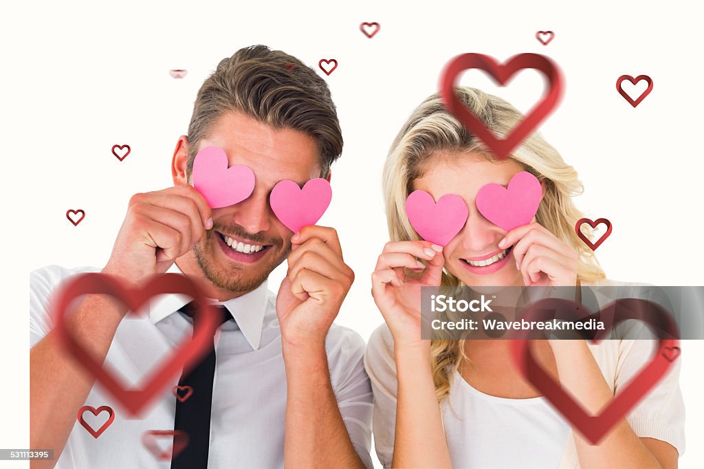 Composite image of cute valentines couple Attractive young couple holding pink hearts over eyes against hearts 18-19 Years Stock Photo