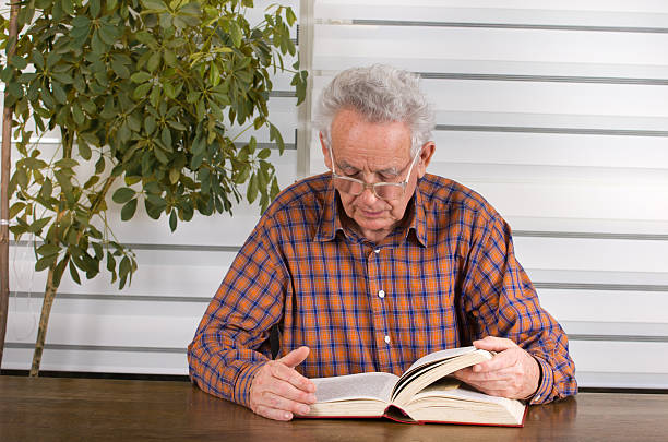 Man reading book Old man with reading glasses reading book in his library late boomer books stock pictures, royalty-free photos & images