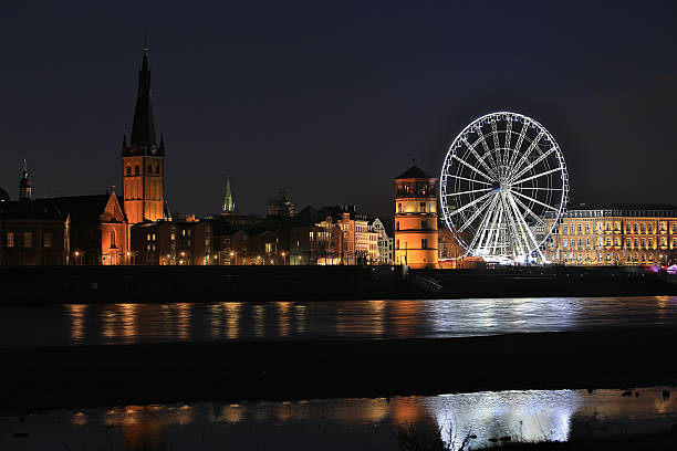 Dusseldorf cityscape along the rhine with a nightview on the old town, St. Lambertus church and a giant Ferris Wheel at the Christmas market on Burgplatz.