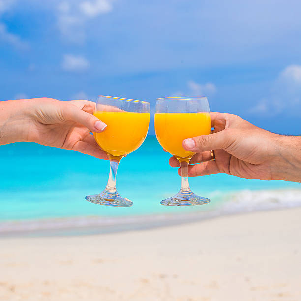 istock Two hands hold glasses with orange juice background blue sky 531135251