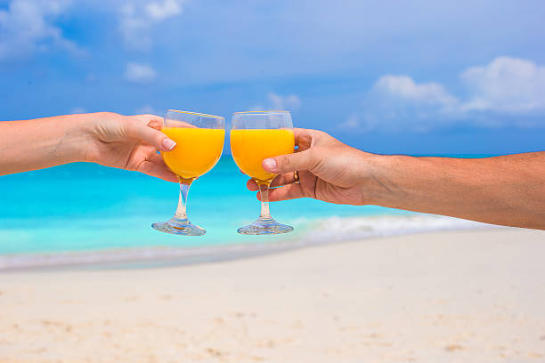 istock Two hands hold glasses with orange juice background blue sky 531135253