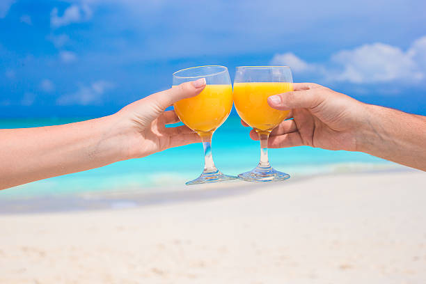 istock Two hands hold glasses with orange juice background blue sky 531135257