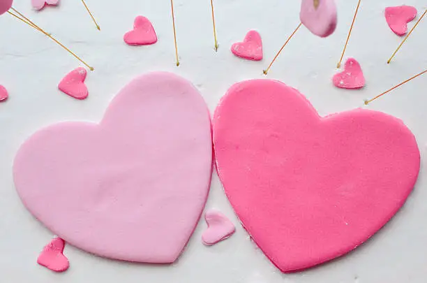 Big red and pink heart and several small marzipan hearts on the surface of the white cream