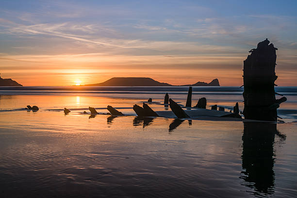 Rhossili Bay Sunset The remains of the Norwegian barque Helvetia and Worm's Head are probably the most photographed points of interest on the whole Gower Peninsula,  South Wales.  They can be found in Rhossili Bay, and can both be seen in this photography. rhossili bay stock pictures, royalty-free photos & images
