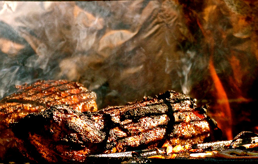 Steaks cooking on the barbecue with fire, flames, grill marks with rotisserie in photograph