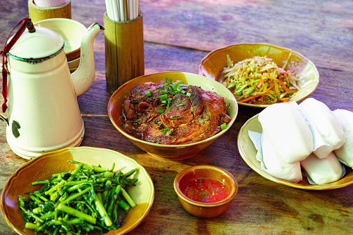 Delicious traditional Chinese braised pig leg with chili sauce with vegetables, steamed Chinese dumplings and Chinese tea at an outdoor Chinese restaurant in Northern Thailand.