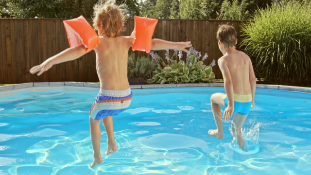 SLO MO DS Two boys jumping into the pool in sunshine
