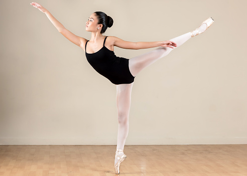 Young classical ballet female dancer practicing ballet in a studio.