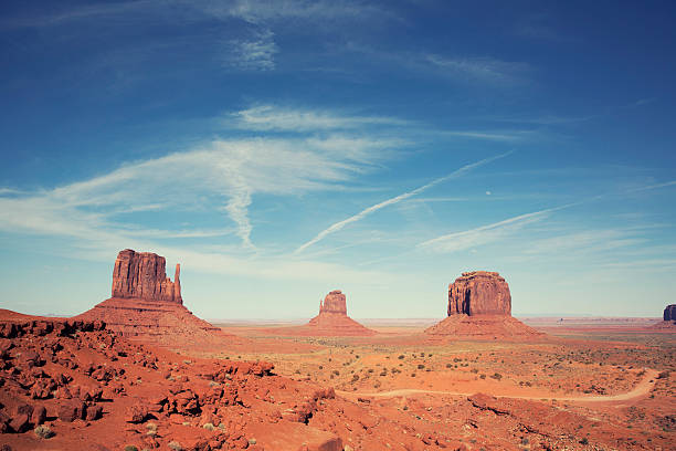 View of East and West Mittens with Merrick's Butte, Monument Valley Arizona, Navajo Indian Tribal Park USA. Taken in the spring with high clouds and jet trails. Cross processed.