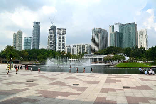 Kuala Lumpur, Malaysia - June 9, 2014: People walking  in The KLCC Park, surrounded by tall skyscrapers, a public metro park located in the vicinity of Petronas Twin Towers