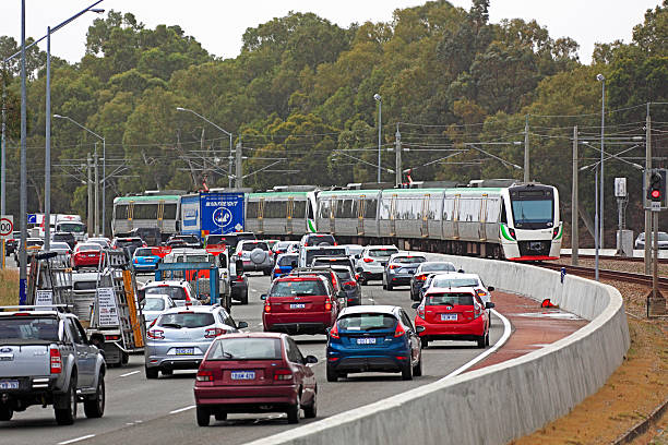 Metro train running down the middle of a congested freeway Perth, Australia - November 10, 2014: A city-bound Transperth electric train service from Butler departs Stirling station in peak time leaving in its wake, several lanes of almost stationary cars on the adjacent Mitchell Freeway. The train will travel at up to 130kph with average service speeds as high as 84kph compared to average freeway speeds as low as 20kph at peak times on 100kph-posted freeways. speed limit sign australia stock pictures, royalty-free photos & images