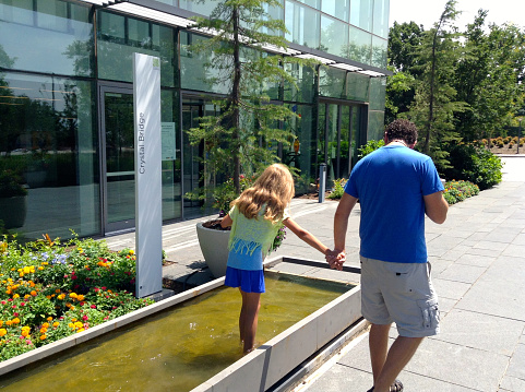 OKC, OK USA - June 14, 2014: Little girl with man walking in a fountain at OKC Myriad Botanical Gardens.