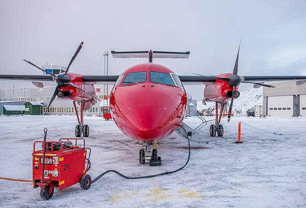Twin engine aircraft is parked in snowy airport in Greenland, connected to ground power. Aircrafts window is repaired after damage.