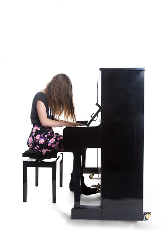 teenage girl plays the piano in studio with white background