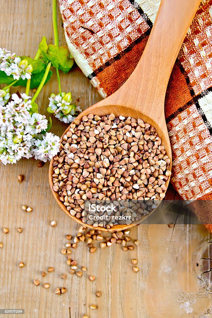 Buckwheat in spoon on board with flower and doily Buckwheat in a spoon with flower buckwheat, brown checkered doily on a wooden boards background 2015 Stock Photo
