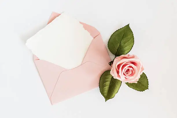 Photo of Pink envelop with white card and rose. Flat lay