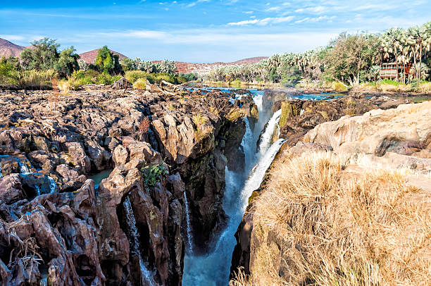 Epupa falls on the border of Namibia and Angola The Epupa Falls (also known as Monte Negro Falls in Angola) are created by the Kunene River on the border of Angola and Namibia, in the Kaokoland area of the Kunene Region. The river is 0.5 km wide and drops in a series of waterfalls spread over 1.5 km, with the greatest single drop being 37 m. The name "Epupa" is a Herero word for "foam", in reference to the foam created by the falling water. kaokoveld stock pictures, royalty-free photos & images