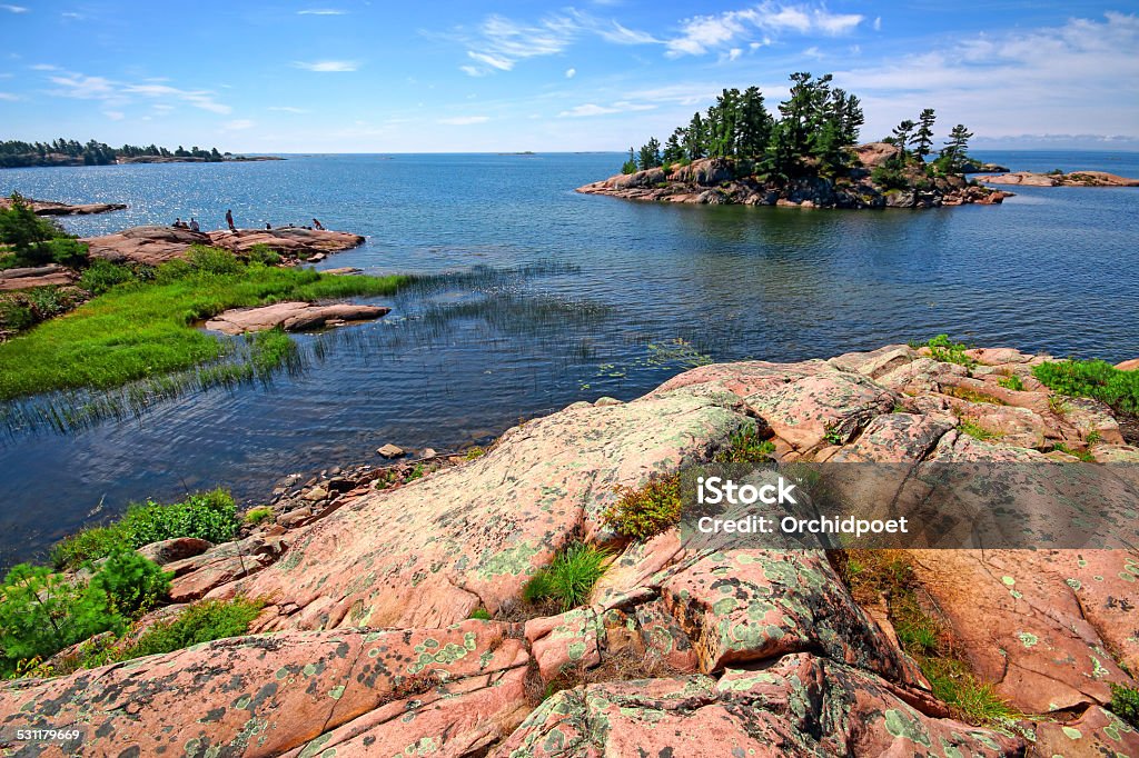 Killarney Provincial Park Rocky shoreline in Killary Provincial Park of Ontario, with wind-swept white pine trees and lichen dotted red granite islands. Unrecognizable group of tourists in the background Ontario - Canada Stock Photo