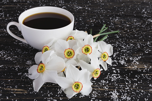 Cup of coffee and narcissus on black wooden background