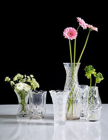 Flowers arranged in crystal vases on black background and white surface