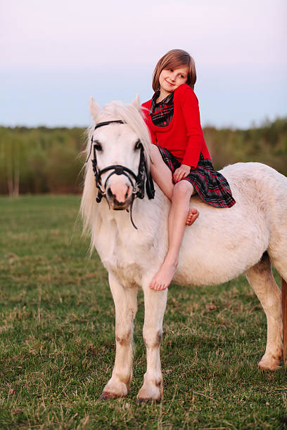 Little young lady barefoot girl sitting on pony and shy stock photo
