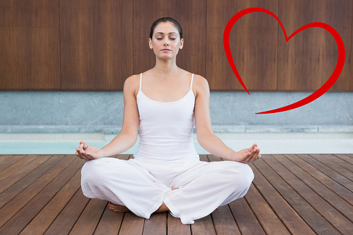 Peaceful woman in white sitting in lotus pose against heart