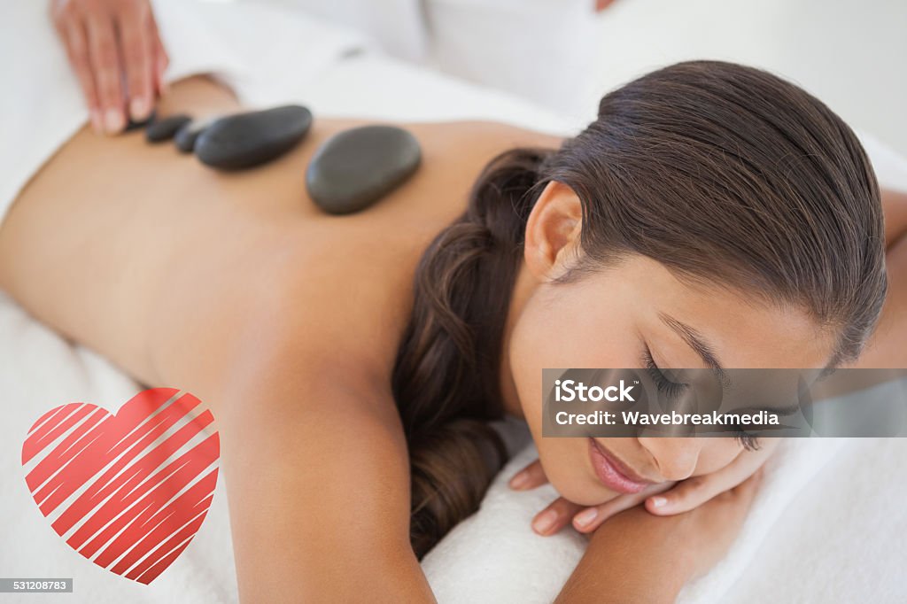 Composite image of beautiful brunette enjoying a hot stone massage Beautiful brunette enjoying a hot stone massage against red heart Massaging Stock Photo
