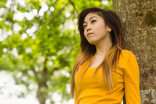 Beautiful young woman standing against tree in the park