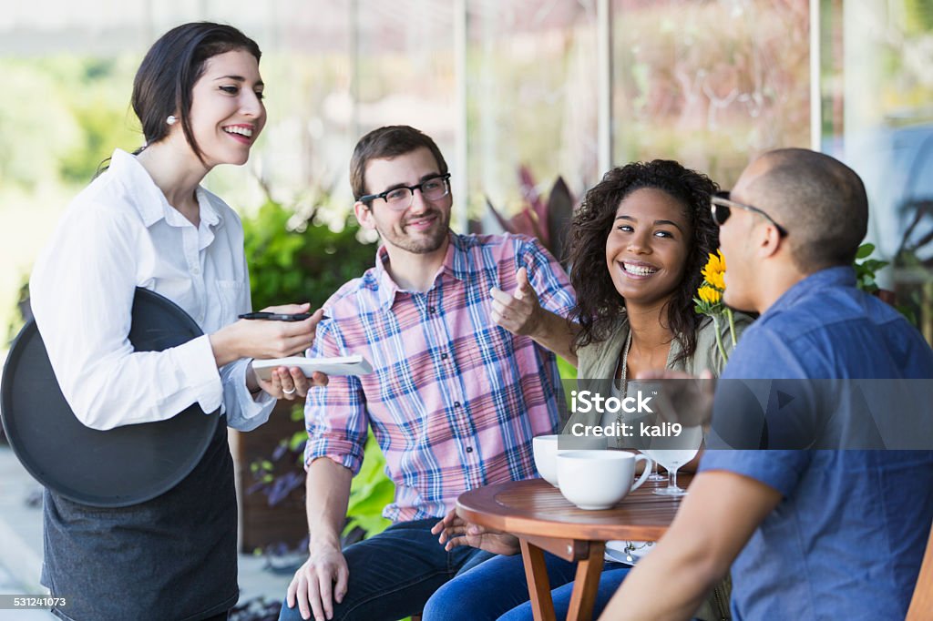 Waitress at sidewalk cafe with customers A waitress at a sidewalk cafe is taking the order of a multiracial group of three friends sitting at a small table.  She is talking to an African American man while his friends watch. Waiter Stock Photo