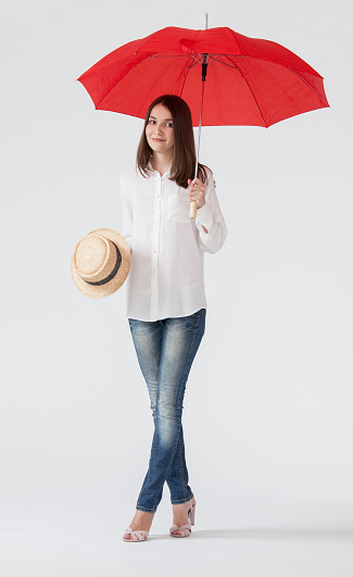Smiling young woman holding a red umbrella and a straw hat, white background