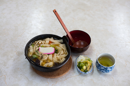 Japanese Udon in hot soup with side dishes on bright background.