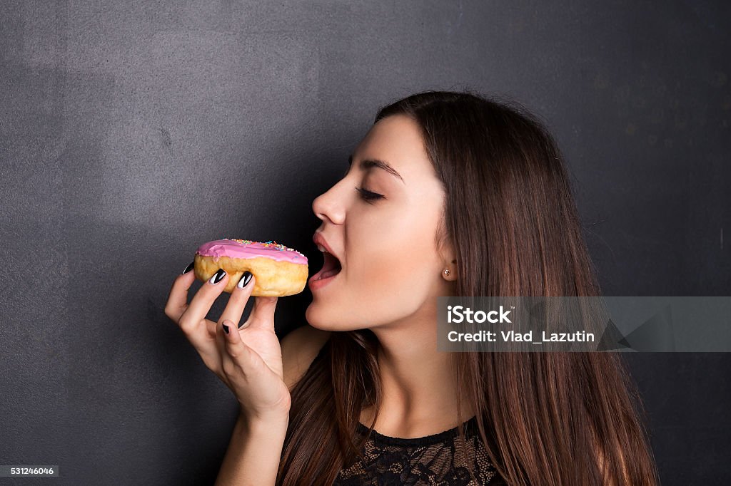 Girl eating a donut Young, attractive girl eating a donut, is holding a donut in his hand in front of mouth Doughnut Stock Photo
