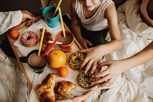Mother serving hot chocolate, fruits, croissants and donuts for her children, still in bed.