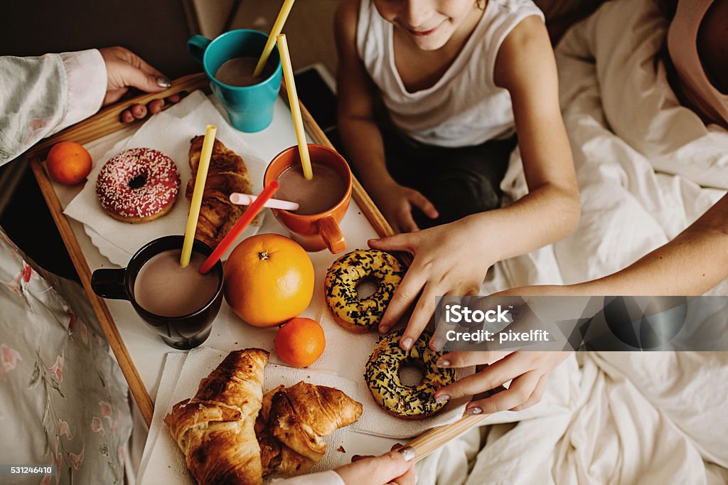 Delicious breakfast Mother serving hot chocolate, fruits, croissants and donuts for her children, still in bed. Breakfast Stock Photo