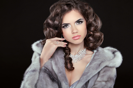 Fashion Beautiful girl with brown long wavy hair, Shine hairstyle with health. Makeup. Jewelry. Fashionable woman in mink fur coat.