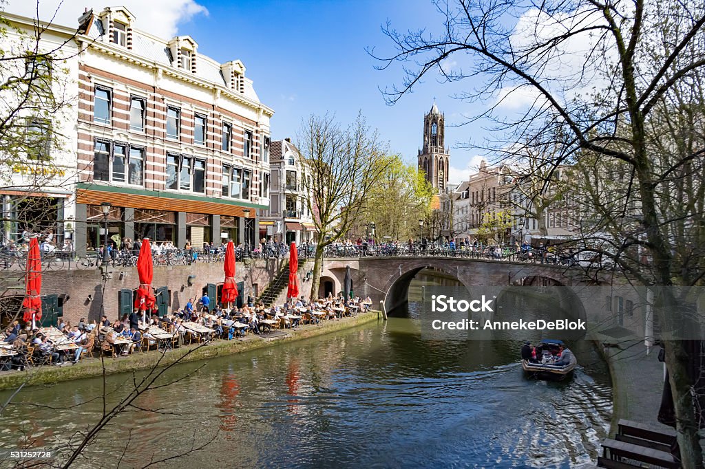 Enyoing Utrecht, The Netherlands All tables at the terraces along the canals in Utrecht are occupied on the first sunny sunday in spring. Many tourist visit this city in The Netherlands. The shops and houses are mostly located  ancient buildings with a nice view on the water. In the background the famous Dom Toren. Utrecht Stock Photo