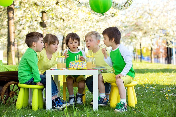 Happy sweet preschool children, celebrating fifth birthday of cu Happy sweet preschool children, friends and relatives, celebrating fifth birthday of cute boy, outdoor in blooming apple tree garden, springtime, late afternoon birthday cake green stock pictures, royalty-free photos & images