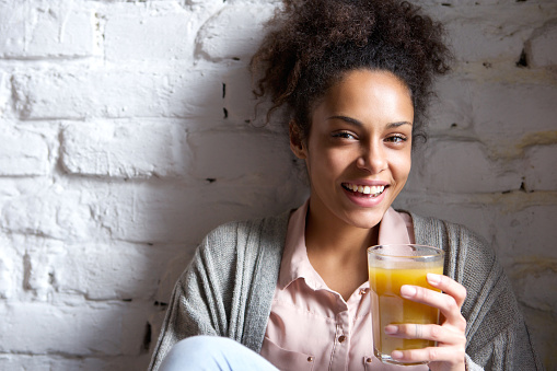 Close up portrait of a beautiful young woman smiling with orange juice