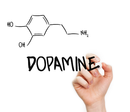 Human hand writing Dopamine chemical formula. Dopamine is a “pleasure” hormone and is stimulated when we strive towards a goal.