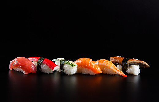 Colorful nigiri sushis in a row on black background