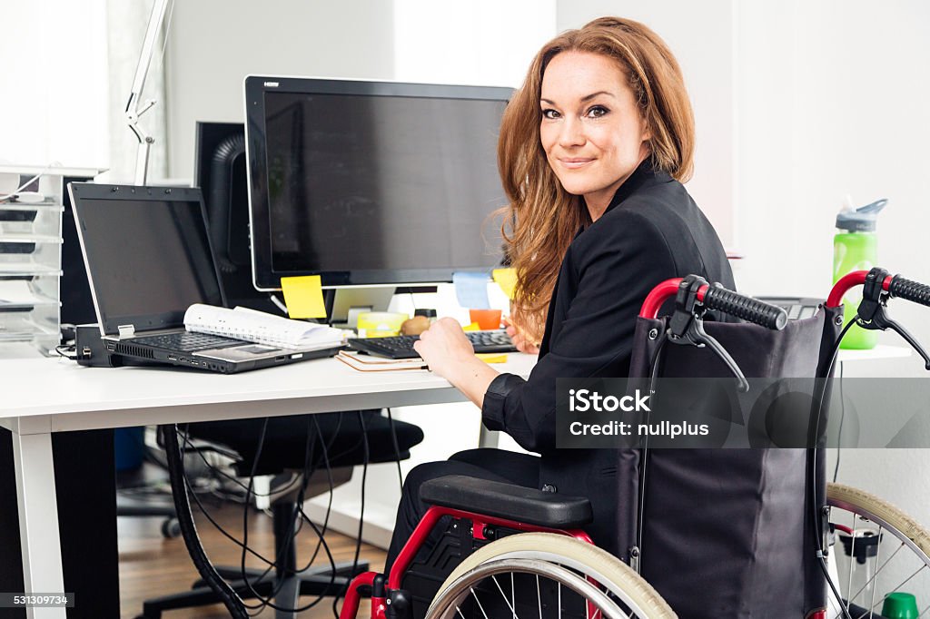 Mujer sentada en el trabajo en oficina moderna silla de ruedas - Foto de stock de Trabajar libre de derechos