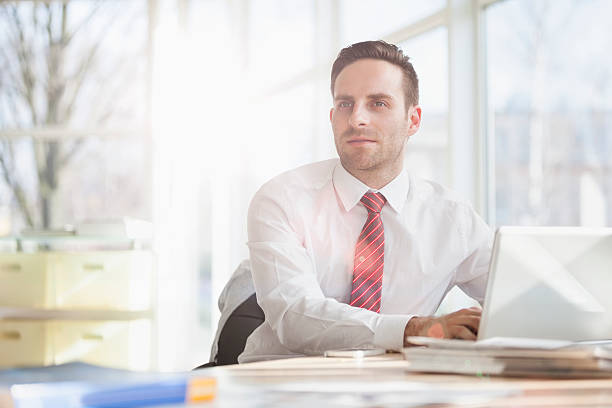 istock Young businessman looking away while using laptop at office desk 531310278