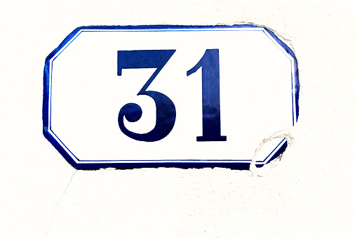 Blue and white vintage ceramic number 31 street address tile on an old white wall, with lots of copy space. Shot in Italy.